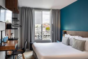 Una habitación de hotel con una cama, un escritorio y una ventana. en Montparnasse Alésia, en París