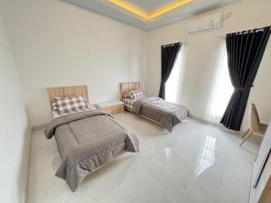 two beds in a white room with windows at Griya Tegalweru Palagan Homestay Jogja in Ngaglik