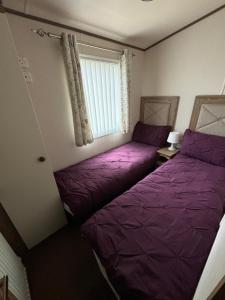 2 Betten in einem Zimmer mit violetter Bettwäsche und einem Fenster in der Unterkunft The Retreat 34, Central Heating, Pet friendly, WiFi - Golden Palm Resort - Meadow Lakes Caravan & Lodge Hire in Chapel Saint Leonards