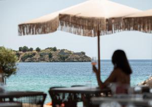a woman sitting at a table with an umbrella overlooking the water at Oniro Boutique Hotel in Toroni