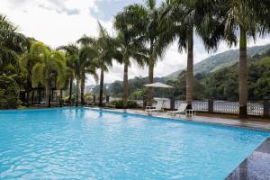 a swimming pool with palm trees and mountains in the background at Casa Rio Resorts Athirappilly in Athirappilly