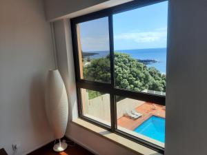 a window with a view of a swimming pool and the ocean at Populo Beach Apartment in São Roque