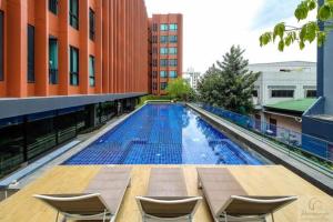 a large swimming pool with chairs on a building at brown condo Phahon67 in Ban Chuat Plai Mai