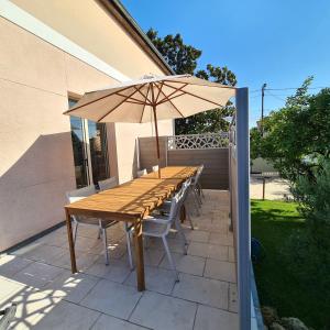 un tavolo in legno con sedie e un ombrellone su un patio di Agréable Villa à mi-chemin de Paris & Disneyland & Stade de France a Gagny