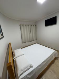 a bedroom with a white bed and a flat screen tv at Bica Conveniência e Hotel in Urupês