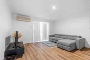 a white living room with a couch and a tv at Shades Of Summer 50 Park Street in Evans Head