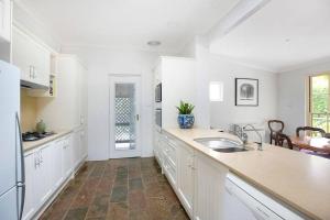 a large kitchen with white cabinets and a sink at Merri Cottage in Bowral +8 photos