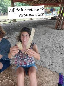 une femme assise sur la plage tenant un morceau de maïs dans l'établissement Yawekata Eco Still BlueWater Resort, à Ngunu