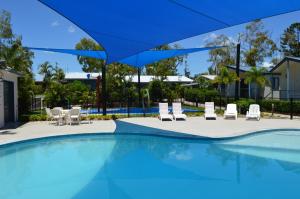 a swimming pool with chairs and a blue umbrella at BIG4 Mackay Blacks Beach Holiday Park in Mackay