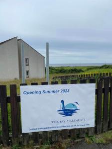 un cartel en una valla que dice abrir los agentes de la bahía de verano en Wick Bay Apartments, en Wick