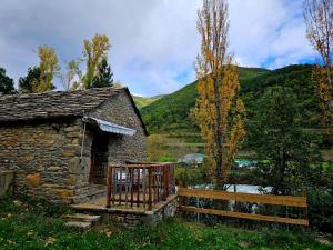 Un antiguo edificio de piedra con un porche de madera junto a un lago. en Camping Ribera del Ara, en Fiscal