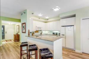 a kitchen with white cabinets and a bar with stools at Beach Colony East Navarre 3A in Navarre