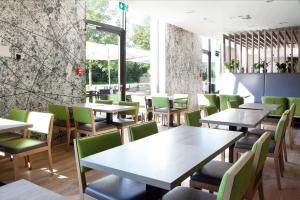a restaurant with wooden tables and green chairs at Holiday Inn Express Friedrichshafen by IHG in Friedrichshafen
