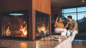 um homem e uma mulher sentados em frente a uma lareira em Corona Dolomites Hotel em Andalo