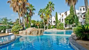a pool with palm trees in front of a building at Cala Menorca in Cala'n Porter