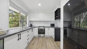 a kitchen with white cabinets and a large window at Boronia Oasis - Tranquil Oasis By The Creek, Sleeps 4 in Sawtell