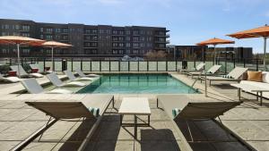 a swimming pool with lounge chairs and tables and a building at Lively Hotel On Oak Oklahoma City, Tapestry By Hilton in Oklahoma City