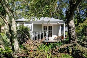 ein kleines weißes Haus mit einer Veranda und Bäumen in der Unterkunft Historic Corinda Cottage in Bundanoon