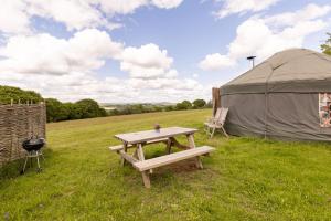 a picnic table and a tent in a field at Cosy-Hilltop-Yurt-StunningViews-Nature-HotTub in Cornworthy +13 photos