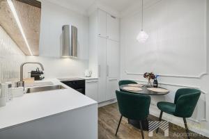 a white kitchen with a table and green chairs at Polonia Residence Glamour by LookAp in Łódź