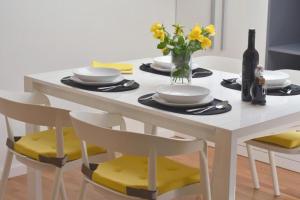 a white dining room table with yellow chairs and a vase of flowers at Apartment Leo in Ploče