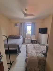 a bedroom with two beds and a tv and a window at Apto perfeito em Arraial do Cabo - Prainha in Arraial do Cabo