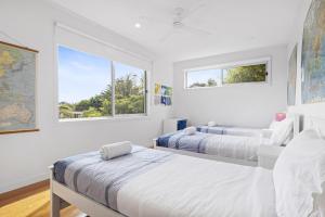 a white bedroom with two beds and two windows at Banksia Beach Retreat in Blairgowrie