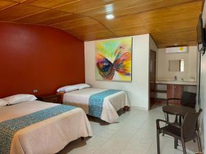 a room with two beds and a table and a painting at Hotel Posada Doña Celes in Mesa Colorada