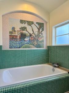 a bath tub in a green tiled bathroom at 源泉かけ流しの一棟貸し温泉宿The Feet Dogo in Matsuyama
