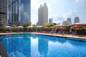 a swimming pool with chairs and umbrellas in a city at Ascott Sathorn Bangkok in Bangkok