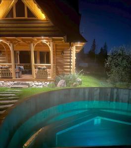 a swimming pool in front of a house at night at Dolina CHOCHOŁOWSKA-drewniany domek z balią in Kościelisko