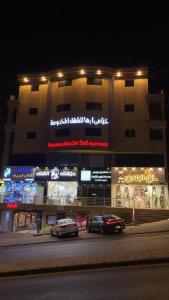 two cars parked in front of a building at night at خزامى ابها للشقق المخدومة in Abha
