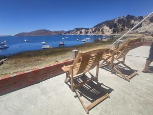 two wooden chairs sitting on a porch overlooking a lake at Hostal Mirador del Sol in Comunidad Challapampa