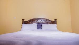 1 cama con cabecero de madera y almohadas blancas en The Urbanite Apartments, en Kitengela 