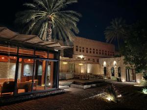 a building with a palm tree behind it at night at Muskad in Al Ḩamrāʼ
