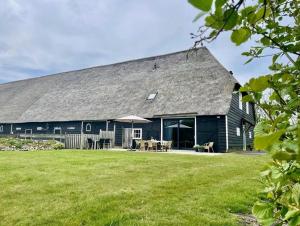 un granero negro grande con césped en Huis aan de vijver, en Kamperland