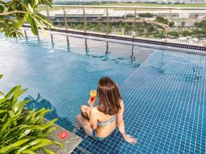 a woman sitting on the edge of a swimming pool at Ibis Saigon Airport in Ho Chi Minh City