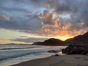 Un grupo de personas de pie en la playa al atardecer en Tahoma Chale Rustico côr Café e vermelho Prumirim Paraiso, en Ubatuba