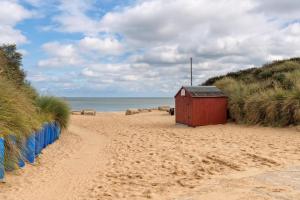 a red shack on a sandy beach next to the ocean at Fantastic Chalet In Hemsby Near To The Beach In Norfolk Ref 18167B in Hemsby +8 photos