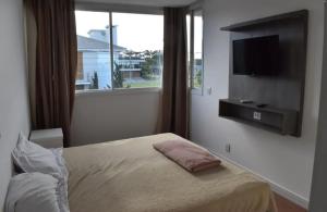 a bedroom with a bed and a tv and a window at Aluguel de Temporada - Dubai Resort Residencial in Capão da Canoa