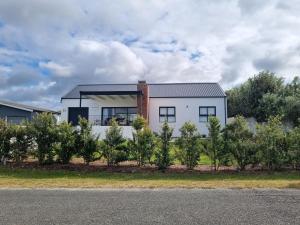 a white house behind a row of trees at Uitwaaien Beach Cottage in Pearly Beach
