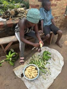 a woman cutting up bananas and a bowl of vegetables at Kibale Cultural Homestay in Fort Portal