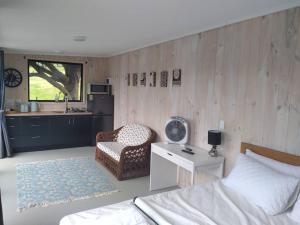 ein Schlafzimmer mit einem Bett und einem Stuhl sowie eine Küche in der Unterkunft Twin Totara Cottage in Mangawhai