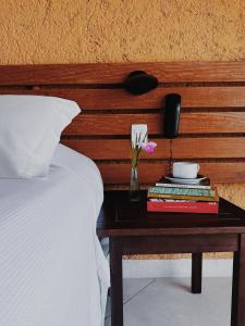 a bed with a nightstand with a table with books at Pousada Mariola in Ilhabela