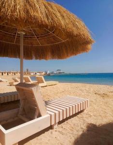 a beach with a straw umbrella and chairs and the ocean at Princess Resort Hurghada in Hurghada