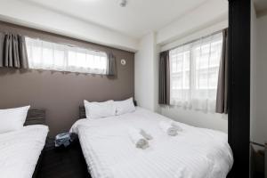 2 bedden in een kamer met witte lakens en ramen bij Estrella in Sapporo