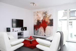 a white living room with two white chairs and a tv at MyWay Hotel & Apartments- Bahnhofstrasse 16 in Wallisellen