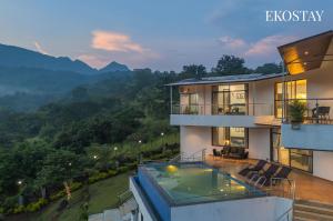 a house with a swimming pool and mountains in the background at EKOSTAY - Infinity Villa with infinity pool in Āmbavna