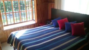 1 dormitorio con 1 cama con almohadas azules y rojas en Cabañas Bosques del Claro, en Pucón