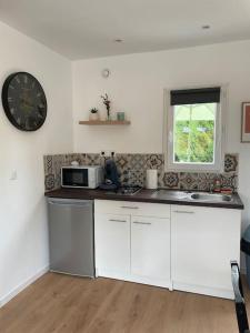 a kitchen with white cabinets and a clock on the wall at Les Chalets du Mancel Chalet Maïka -Bouleries Jump - 24h du Mans in Parence